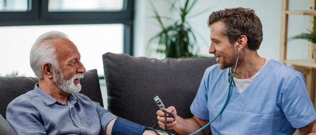 Happy general practitioner measuring blood pressure of mature man while being in a home visit.
