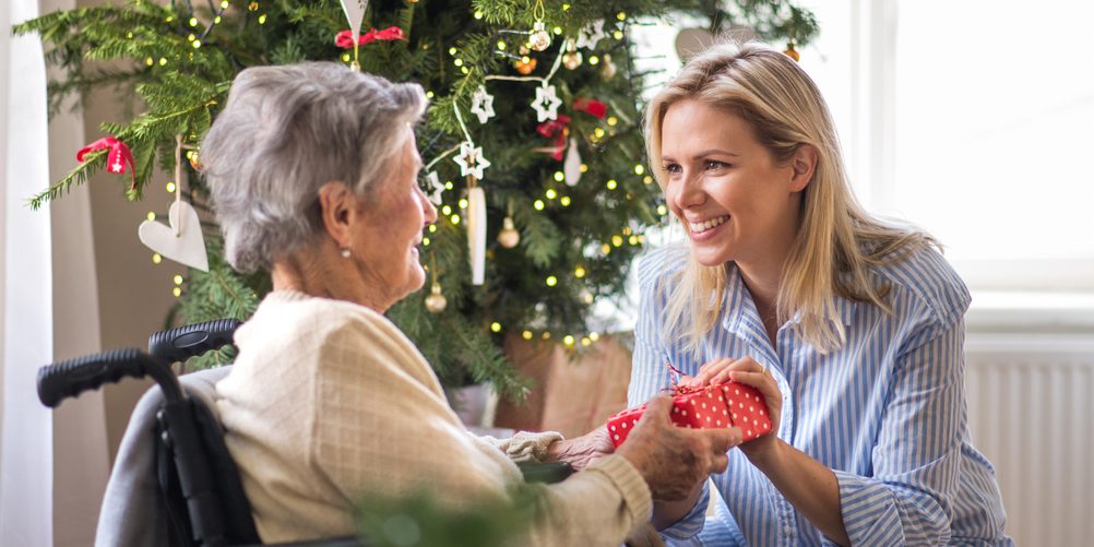 A health visitor and a senior woman in wheelchair with a present at home at Christmas time.