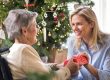 A health visitor and a senior woman in wheelchair with a present at home at Christmas time.