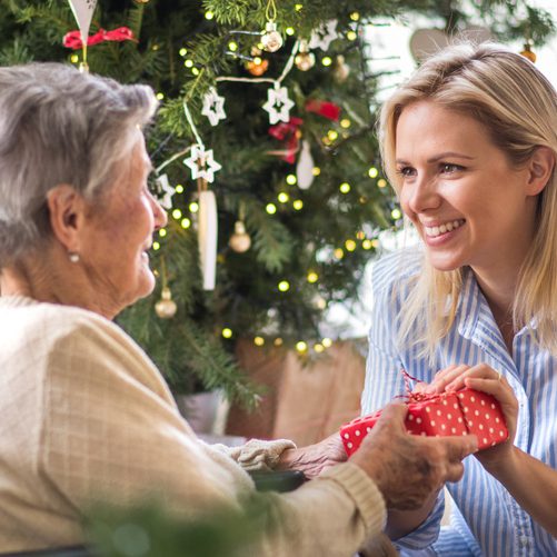 A health visitor and a senior woman in wheelchair with a present at home at Christmas time.