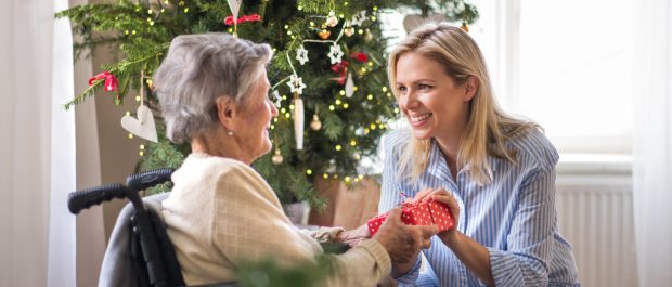 Health visitor and senior woman in wheelchair with a present at home at Christmas. A health visitor and a senior woman in wheelchair with a present at home at Christmas time.