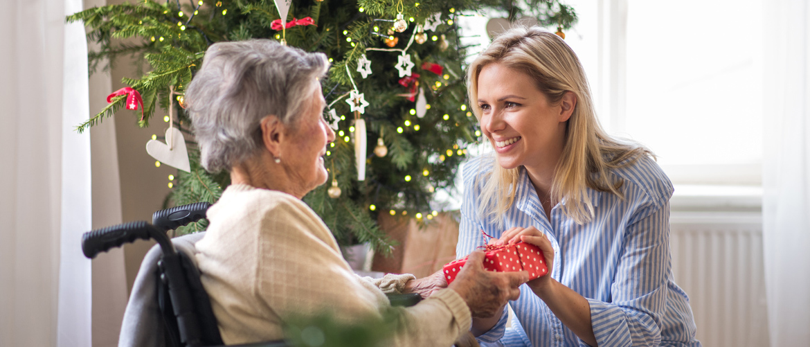 A health visitor and a senior woman in wheelchair with a present at home at Christmas time.