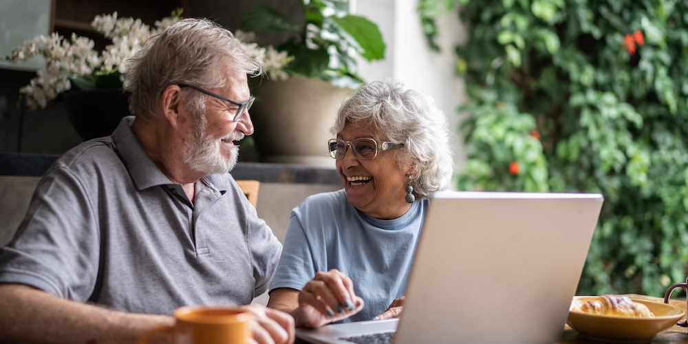 Elderly couple at table looking at laptop