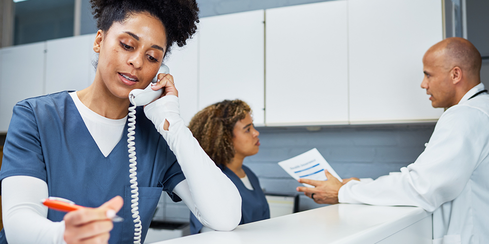 Nurse on phone while doctor and other nurse talk behind her.