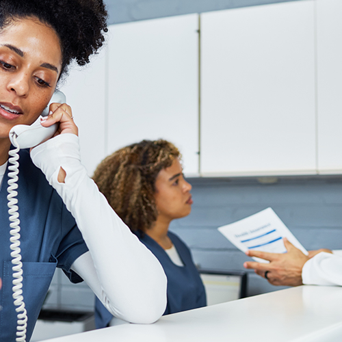 Nurse on phone while doctor and other nurse talk behind her.