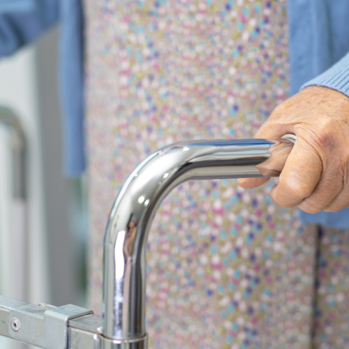 Elderly person grips a chrome walker to support walking and balance.