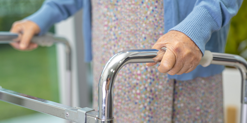 Fall Prevention Blog Header Elderly person gripping the chrome handles of a rollator walker at the front.